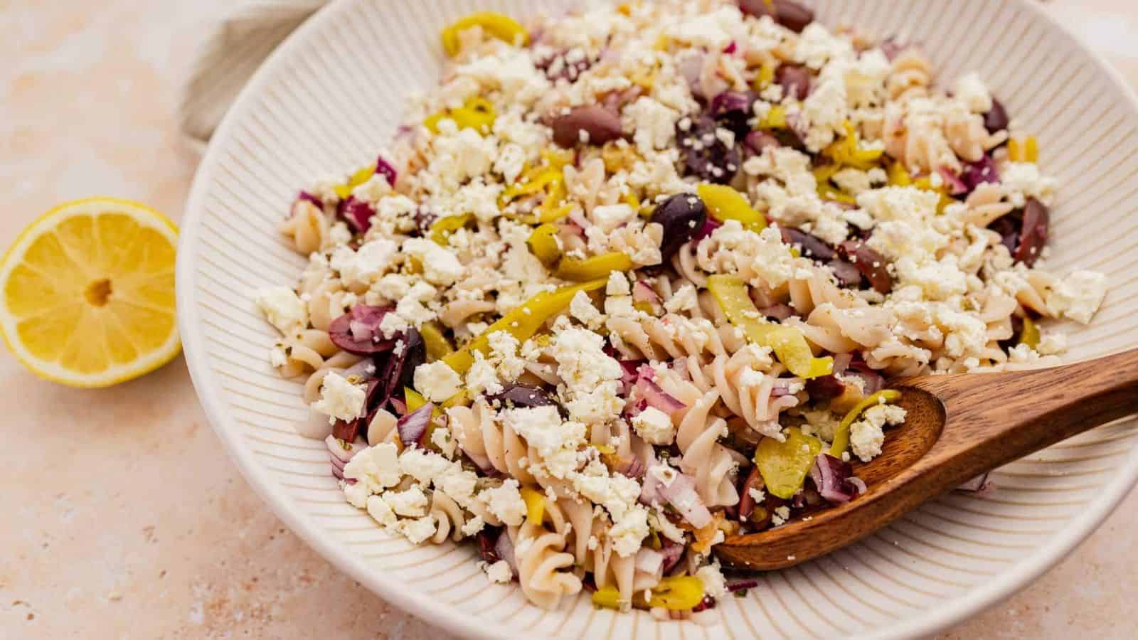 Lemon greek pasta salad in a white bowl with a wooden spoon.