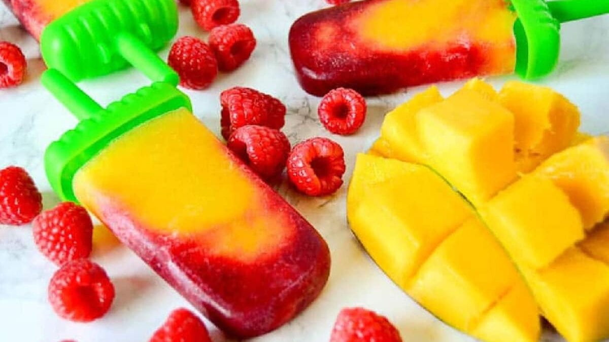 Raspberry mango popsicle on a marble background next to raspberries and mango.