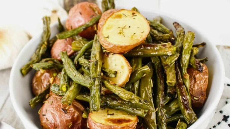 A bowl of roasted red potatoes and green beans seasoned with herbs.