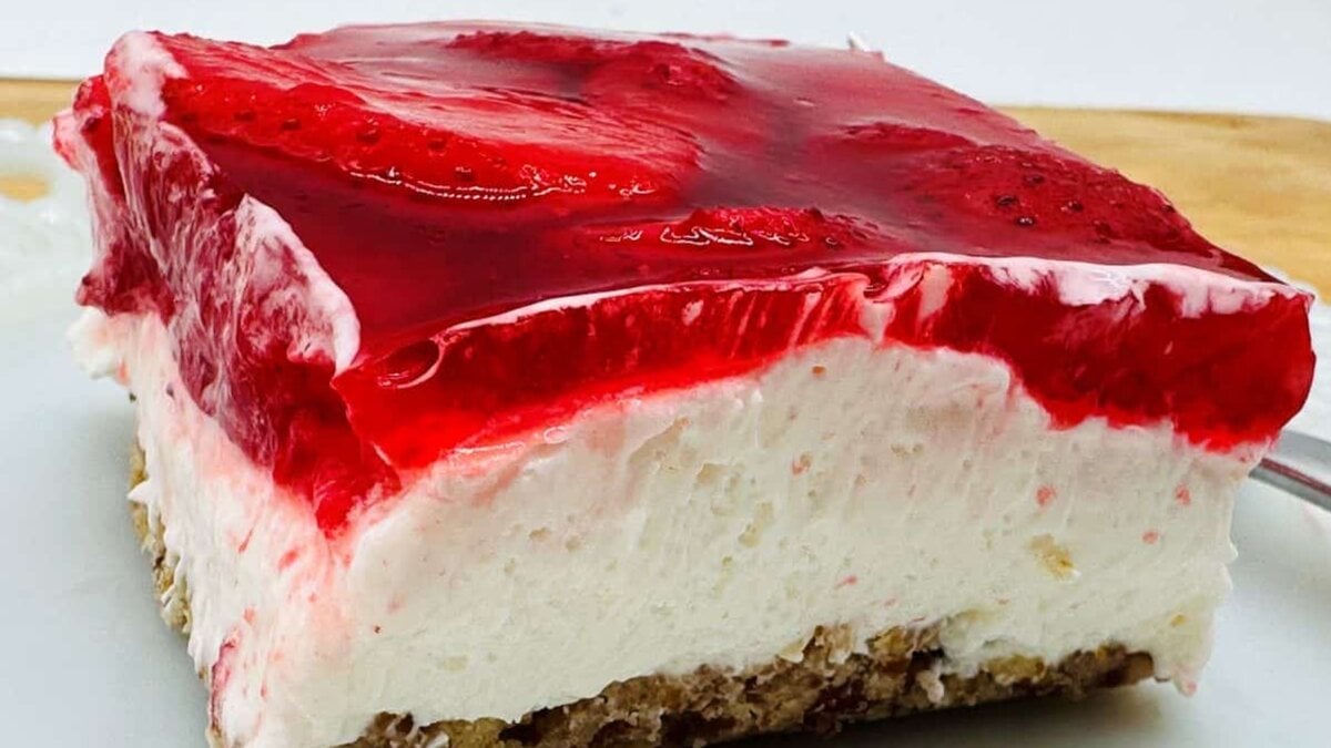 Slice of strawberry pretzel dessert with a layer of strawberries in gelatin, cream cheese filling, and crunchy pretzel crust on a white plate.