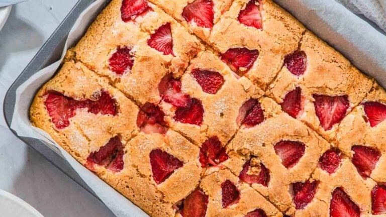 A rectangular baking dish filled with golden-brown strawberry cake, cut into squares, with visible pieces of strawberries on top.