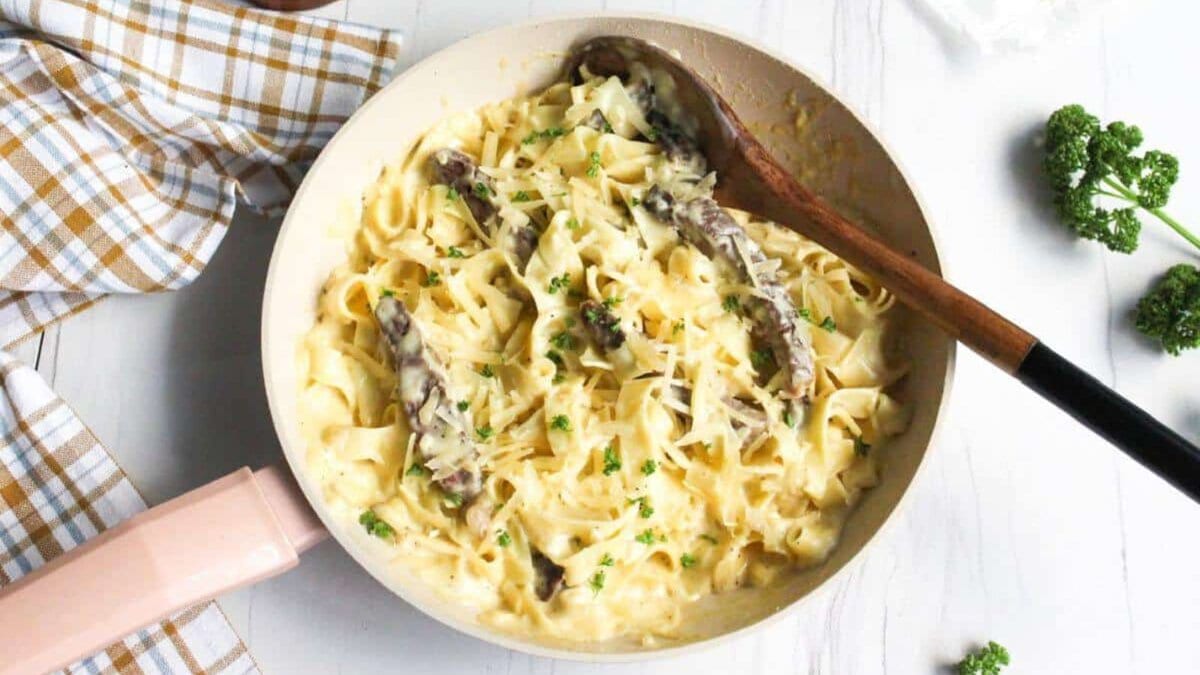 Alfredo steak pasta in skillet with wooden spoon.