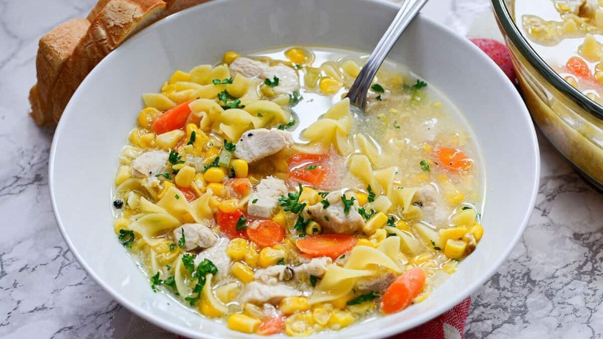 Chicken corn noodle soup in bowl with spoon.
