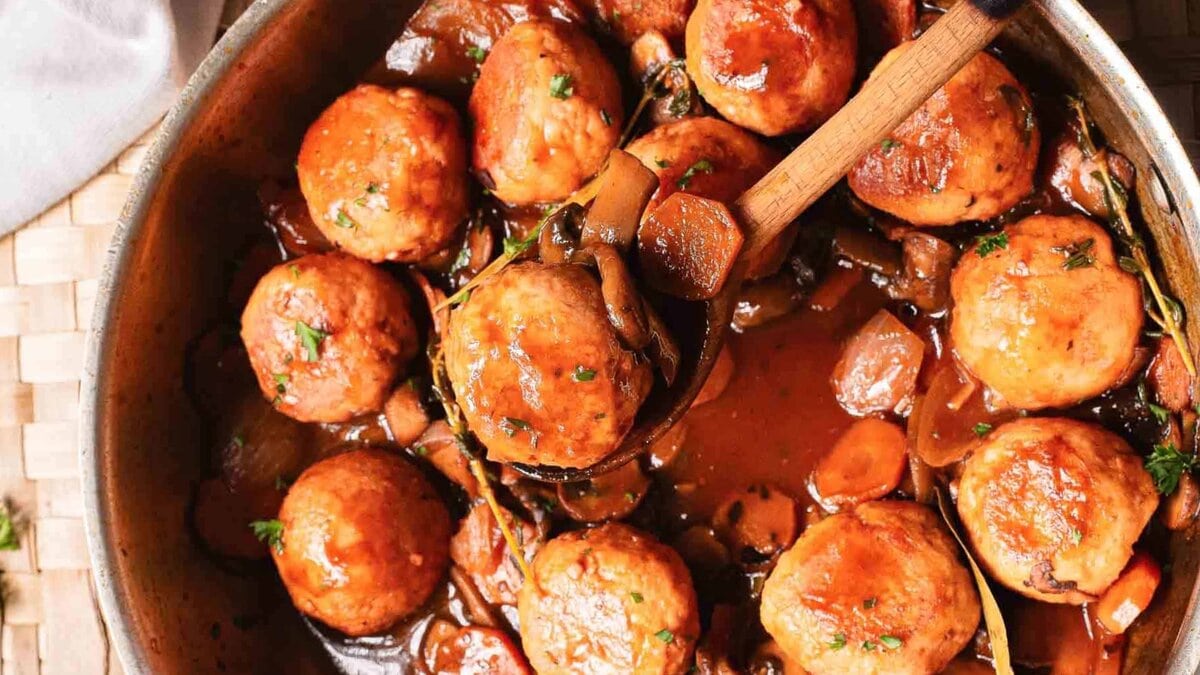 A skillet of glazed meatballs in sauce with mushrooms and herbs, viewed from above.