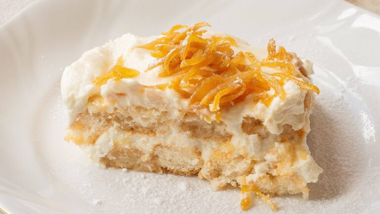A slice of layered dessert with cream and grated orange zest on top, served on a white plate.