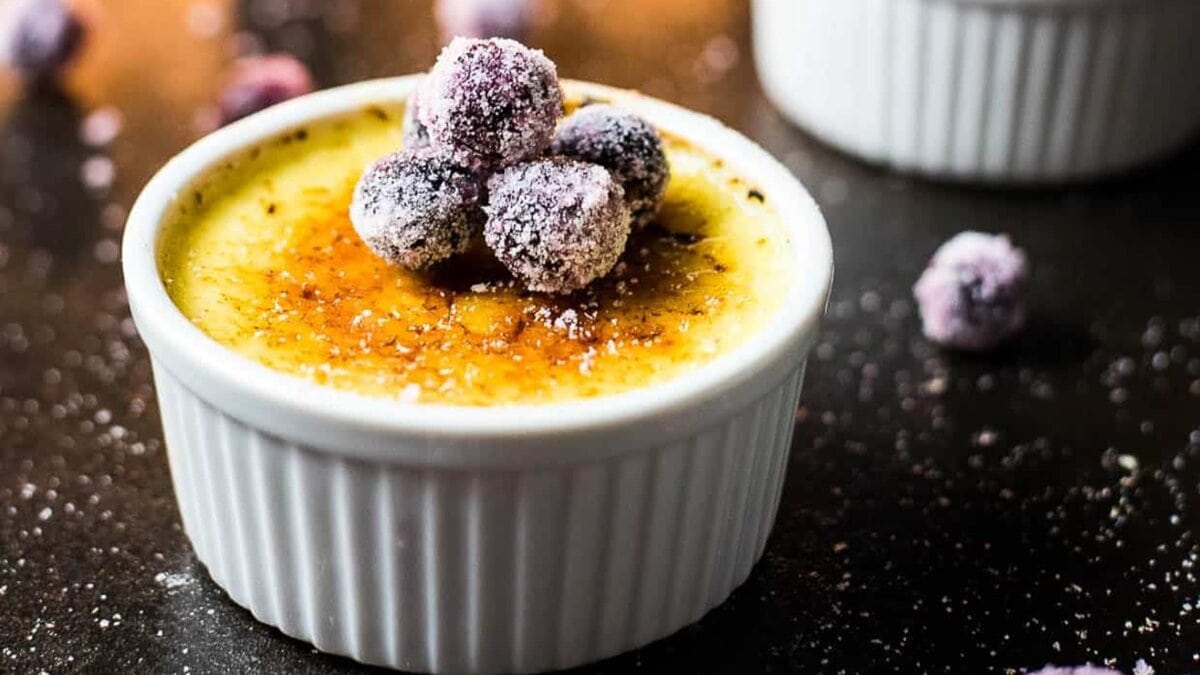 A serving of eggnog creme brulee with sugared cranberries on top.