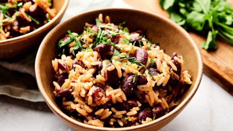 A bowl of cooked rice mixed with red kidney beans and garnished with chopped herbs.