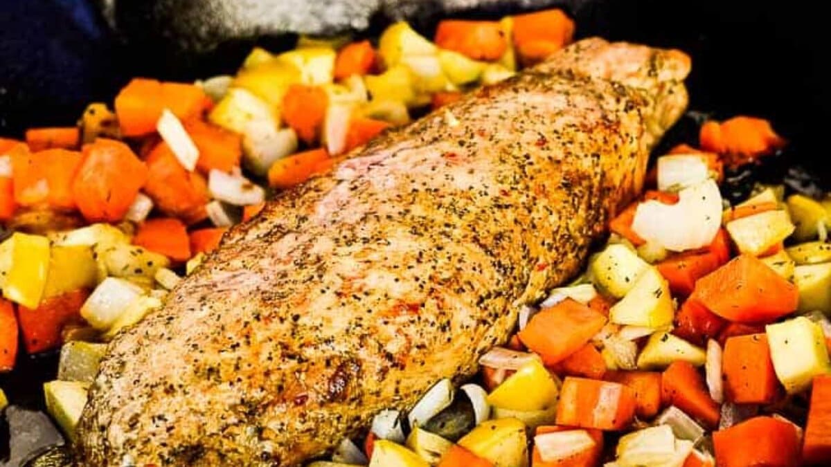 Cooked seasoned pork surrounded by diced vegetables in a black skillet on a wooden table.