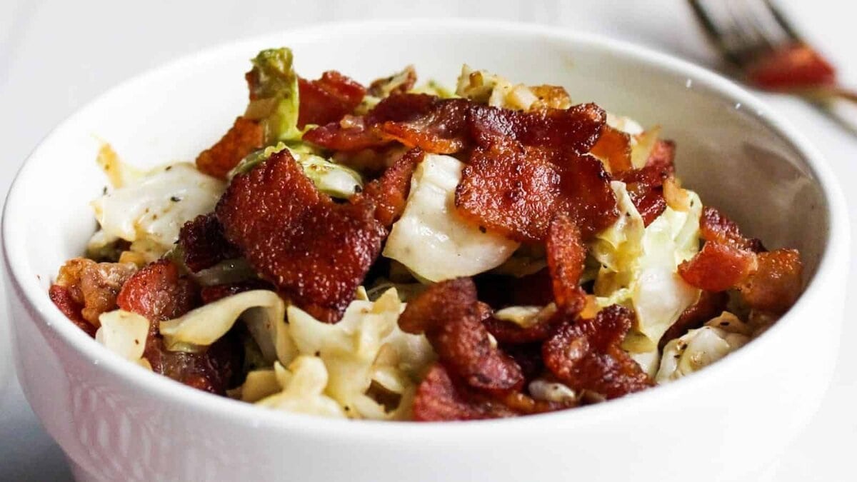 Cabbage and bacon in white serving bowl.