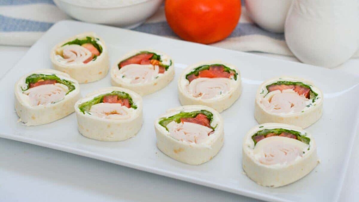 A plate of turkey wraps with tomatoes and lettuce.