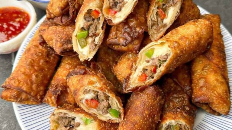 A plate of crispy egg rolls filled with beef, green and red bell peppers, with a small dish of dipping sauce on the side.