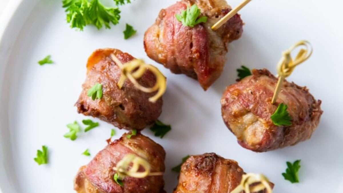 Air Fryer Bacon Wrapped Meatballs on a white plate with parsley and tooth picks.