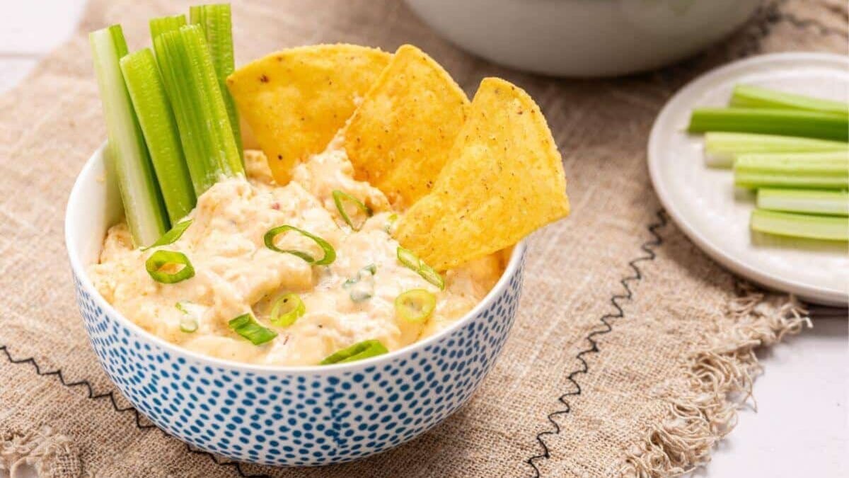 A bowl of buffalo chicken dip with celery and chips.