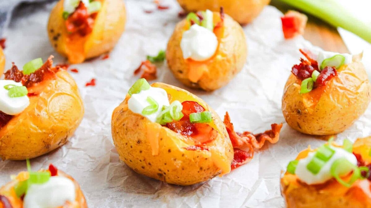 Mini baked potatoes topped with sour cream, bacon bits, cheddar cheese, and chopped green onions.