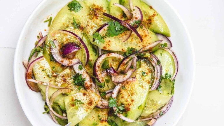 Sliced avocado and red onion salad garnished with cilantro and sprinkled with chili powder on a white plate.