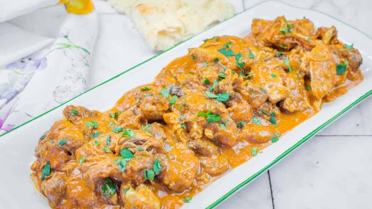 A rectangular plate of Chicken Tikka Masala with herbs on top.