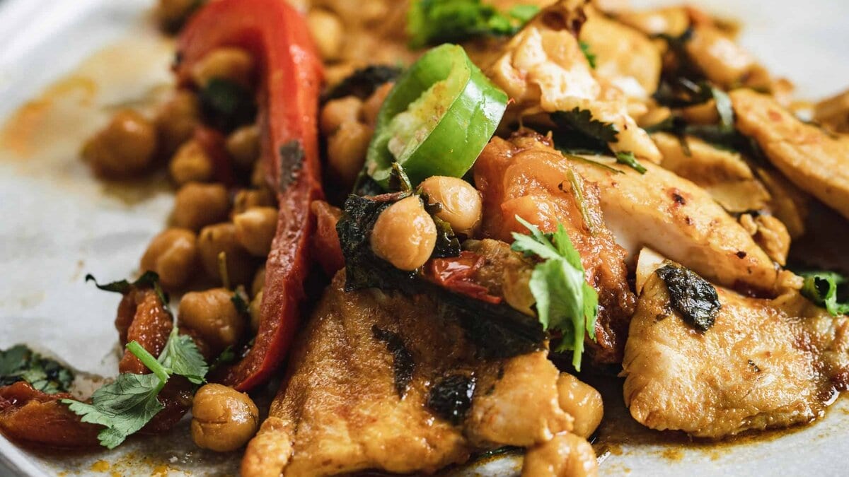 A fork holds a bite of chickpea stew with herbs above a pot filled with stew, chickpeas, and greens.