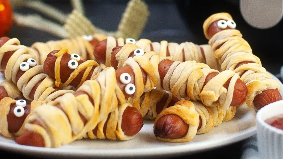 Air fryer mummy hot dogs wrapped in dough with candy eyes on a tray for Halloween.
