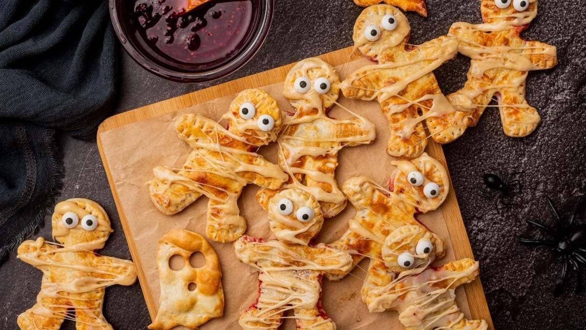 Halloween mummy hand pies drizzled with icing and candy eyes on a baking tray.