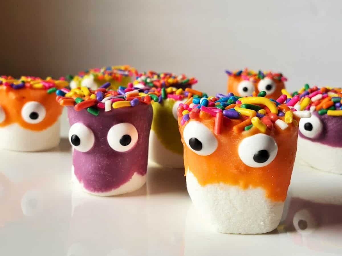 Colorful cake pops and marshmallows with googly eyes and sprinkles on a white plate.