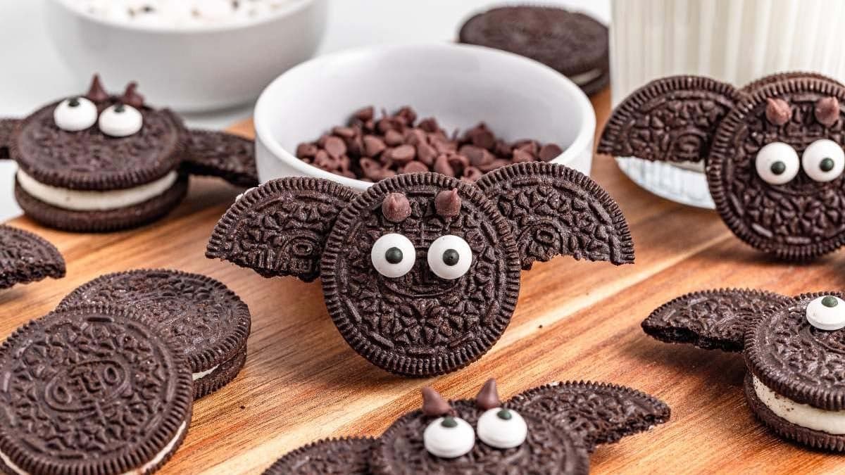 Oreo bat cookies with candy eyes and chocolate wings arranged on a dark surface.