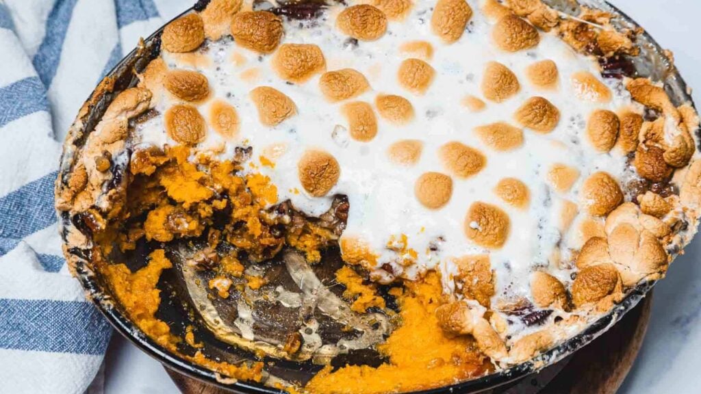 A partially eaten sweet potato casserole topped with toasted marshmallows in a round baking dish.