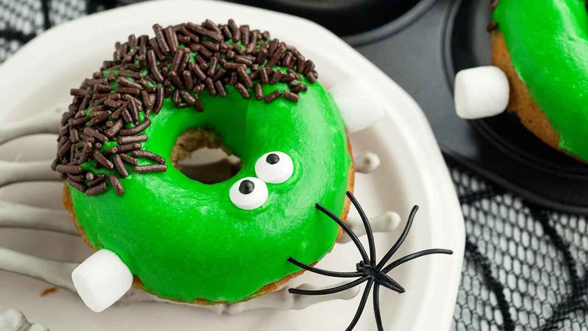 Green Frankenstein donuts with chocolate hair and candy eyes on a platter.