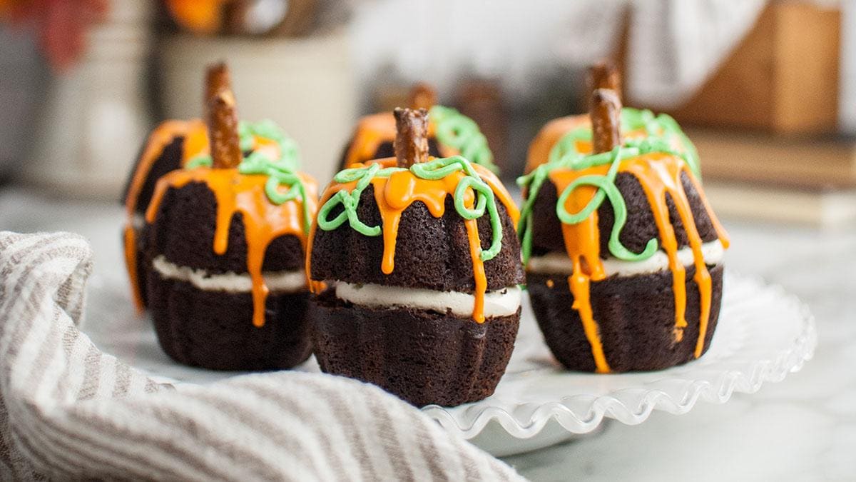 Pumpkin-shaped chocolate mini bundt cakes topped with icing for a Halloween dessert.