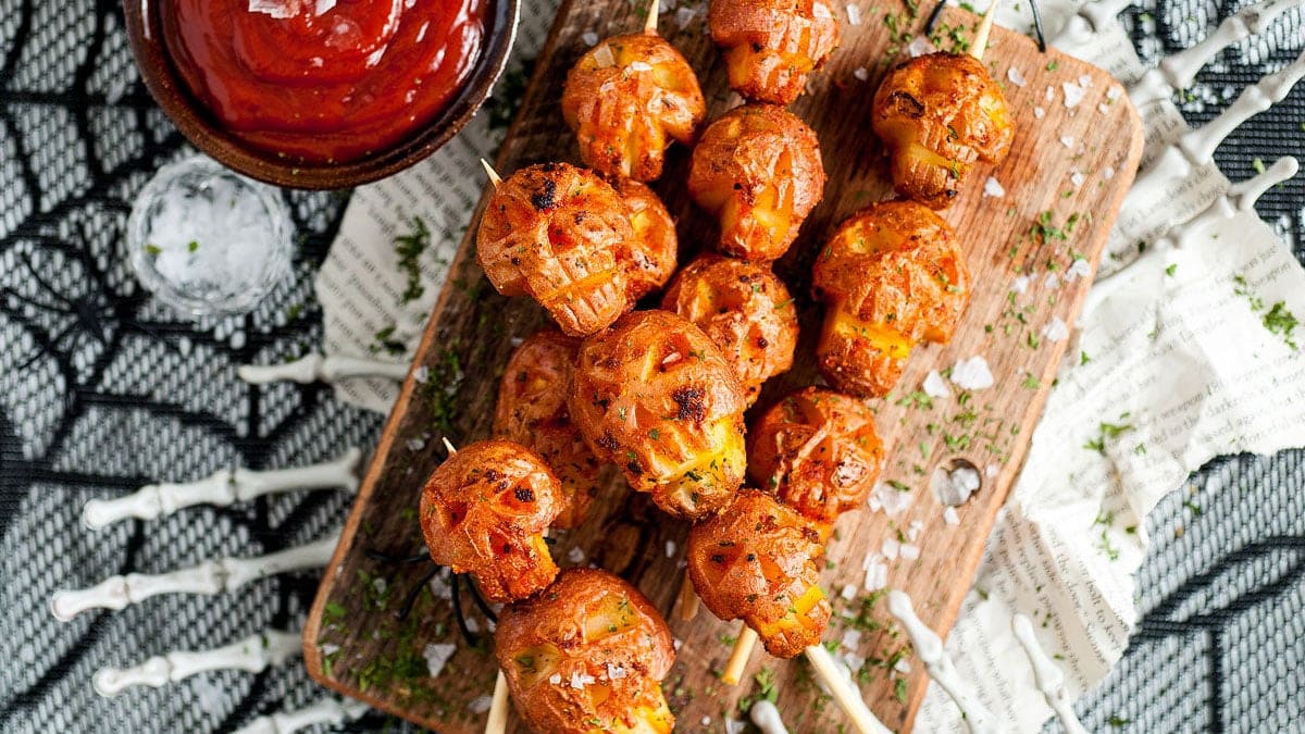 Crispy roasted potatoes shaped like skulls served on a dark tray for a spooky Halloween side dish.