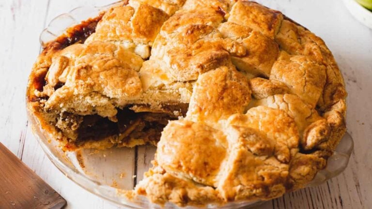A lattice-topped pie with a golden-brown crust sits on a glass pie plate, with one slice removed to reveal a fruit filling—making it a classic choice among easy fruit desserts.