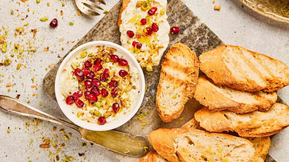 Toasted bread slices topped with creamy cheese, pomegranate seeds, and chopped pistachios.