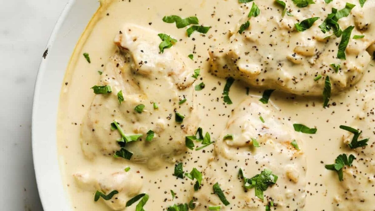 A white skillet of creamy garlic chicken garnished with herbs.