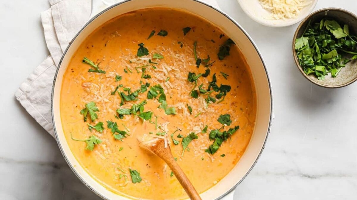 Creamy Italian sausage soup in a pot with a spoon and garnishes on the side.