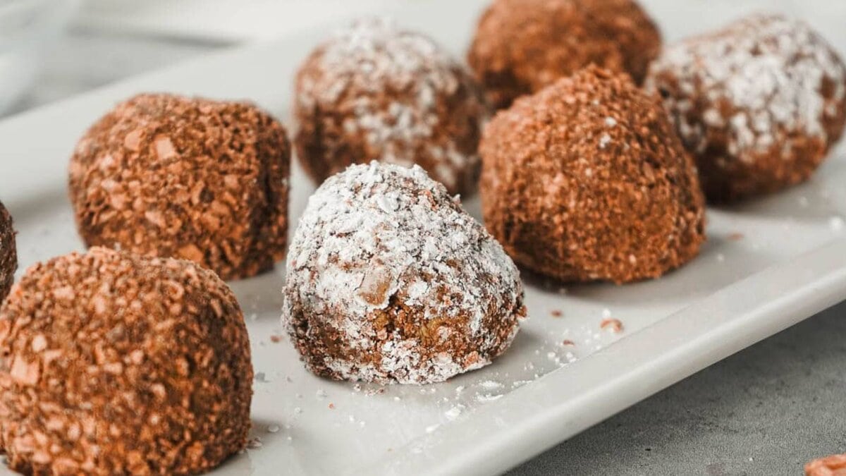 Chocolate truffles dusted with powdered sugar on a white plate, with wafer biscuits beside them.