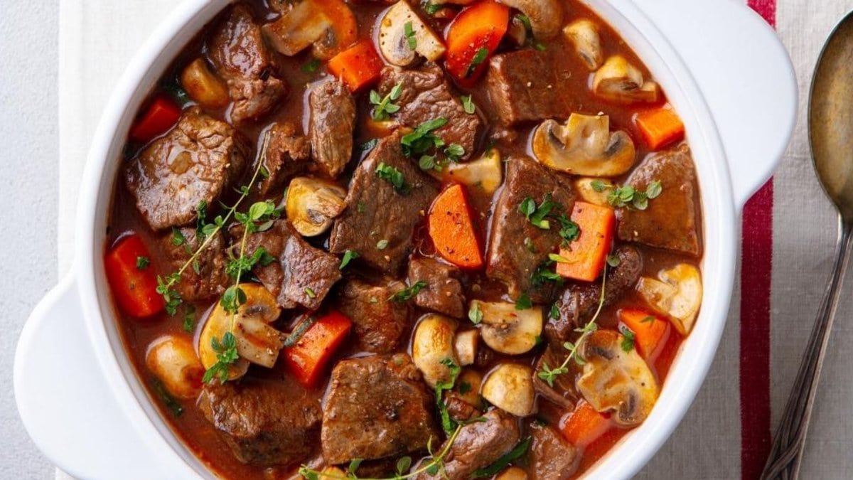 Beef stew in a white pot served with a spoon.
