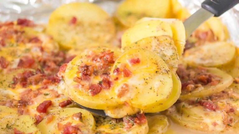 Sliced potatoes baked with melted cheese, bacon bits, and herbs, being served with a spatula.