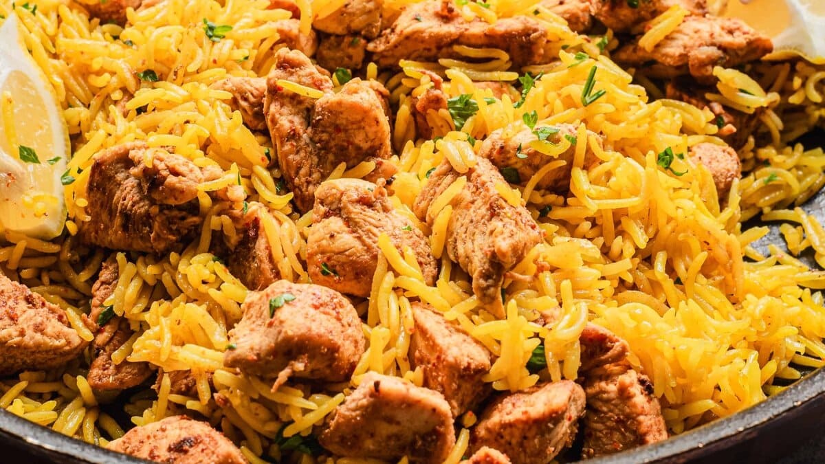 Close-up of seasoned yellow rice mixed with chunks of cooked chicken, garnished with chopped herbs.