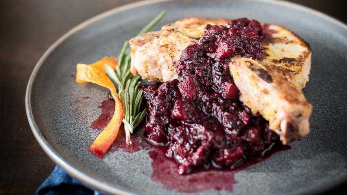 Pork chops with blackberry applesauce on a gray plate.