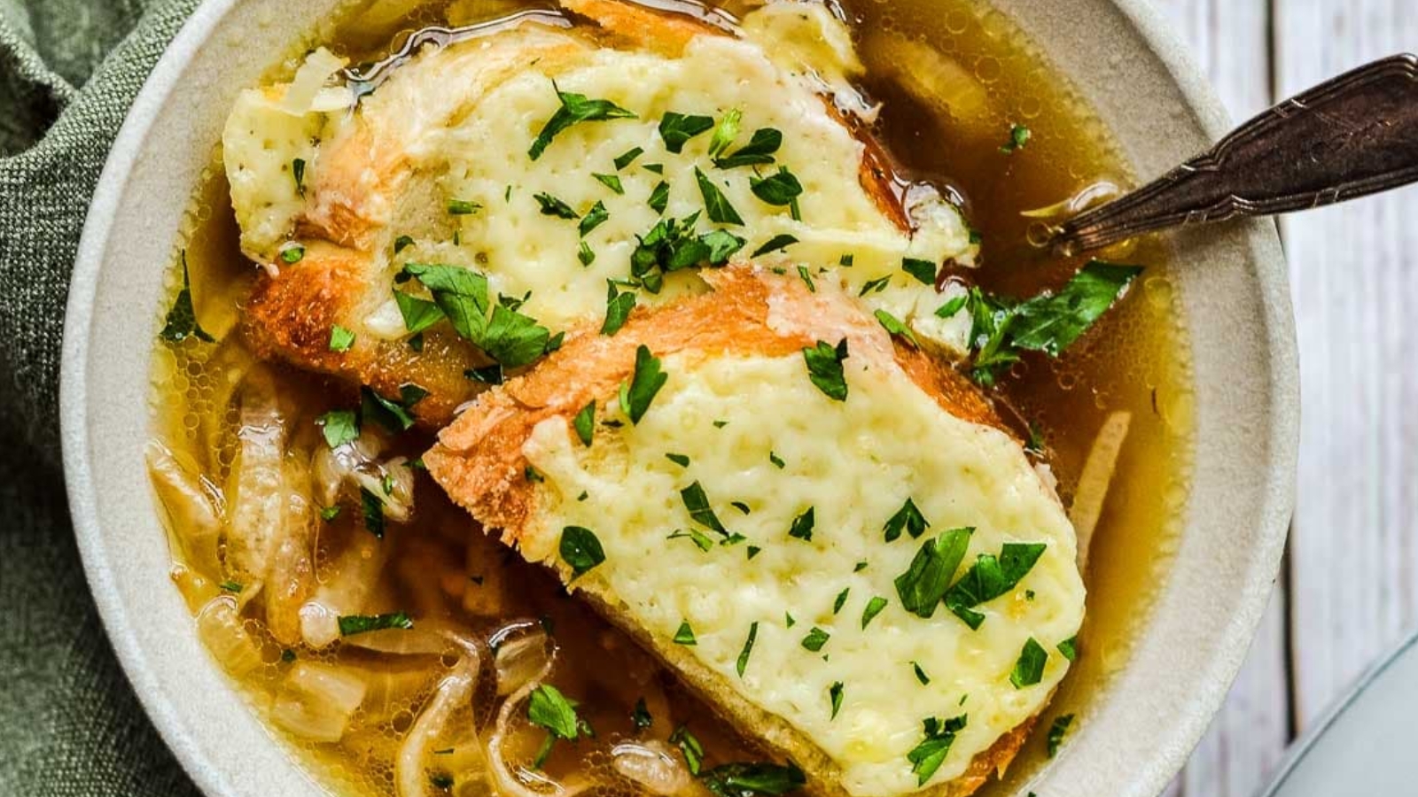 A bowl of French onion soup topped with two slices of toasted bread covered in melted cheese and garnished with chopped parsley.