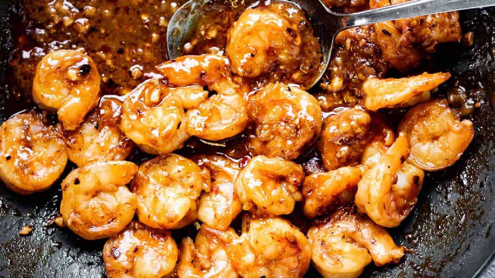 Cooked shrimp coated in a thick, brown garlic sauce with a spoon resting in the pan.