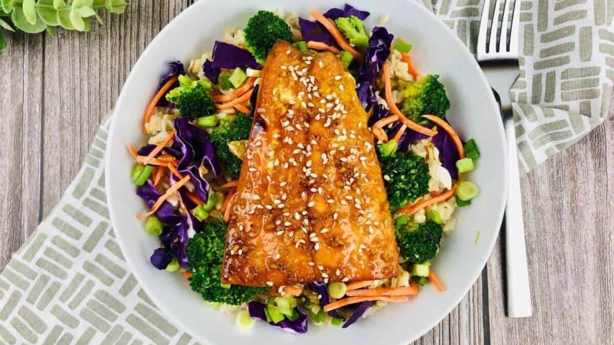 Teriyaki salmon bowl with glazed salmon over rice topped with fresh vegetables.