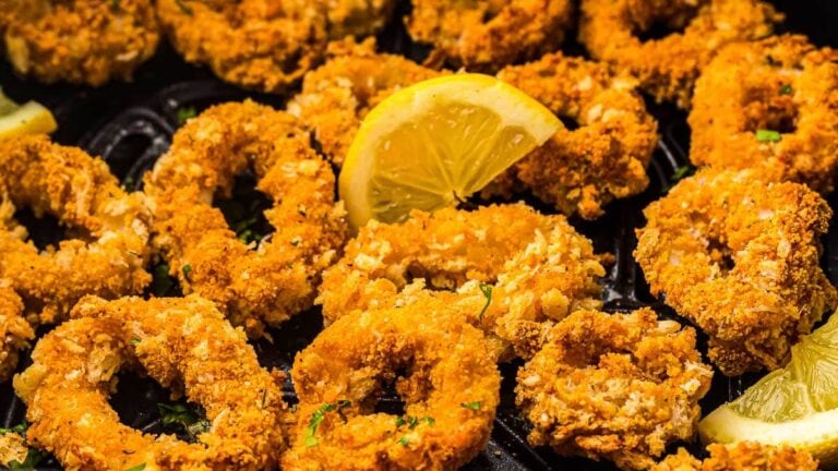 Close-up of crispy fried calamari rings garnished with parsley, served with lemon wedges.