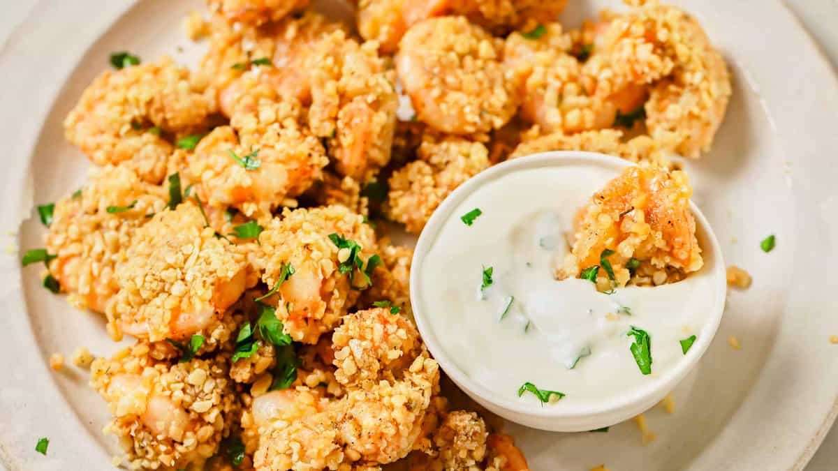 A plate of breaded shrimp garnished with chopped herbs, served with a side of creamy white dipping sauce.