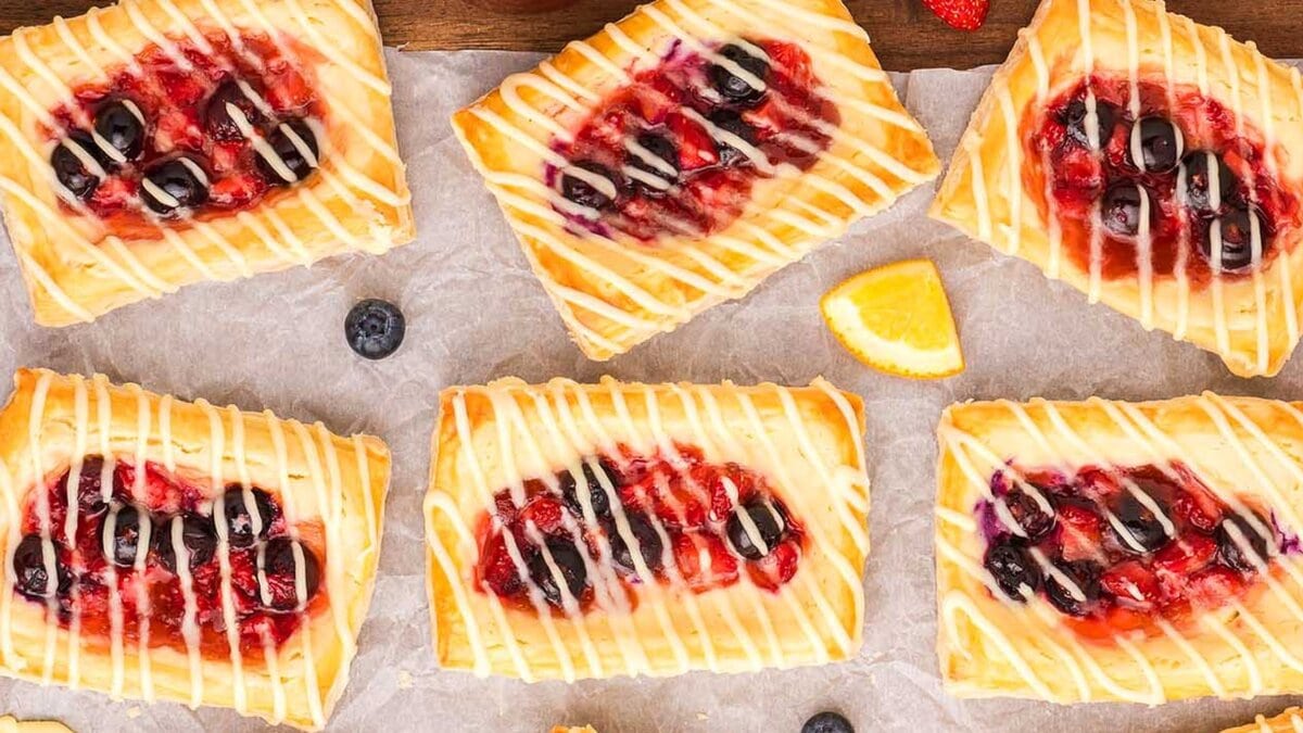 Rectangular fruit danishes with berry filling and white icing drizzle on a wooden tray.