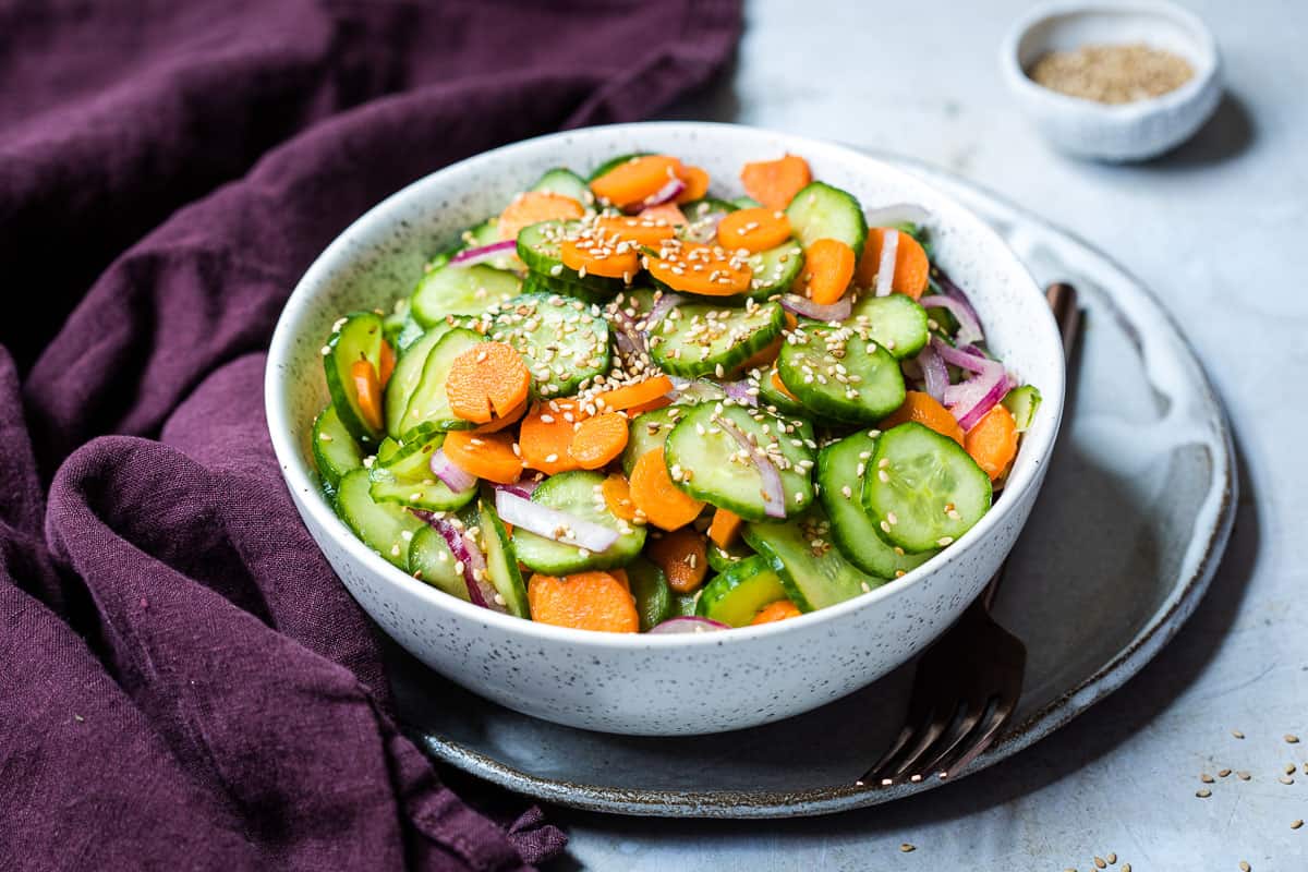 Crisp cucumber and carrot salad with red onion and sesame seeds in a glass bowl.