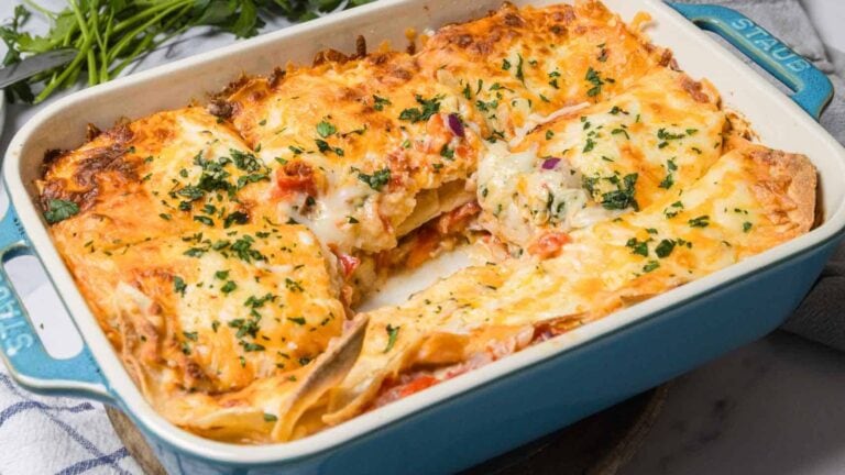 A rectangular baking dish filled with cheesy baked lasagna, with one serving removed, revealing layers of pasta, sauce, and melted cheese.