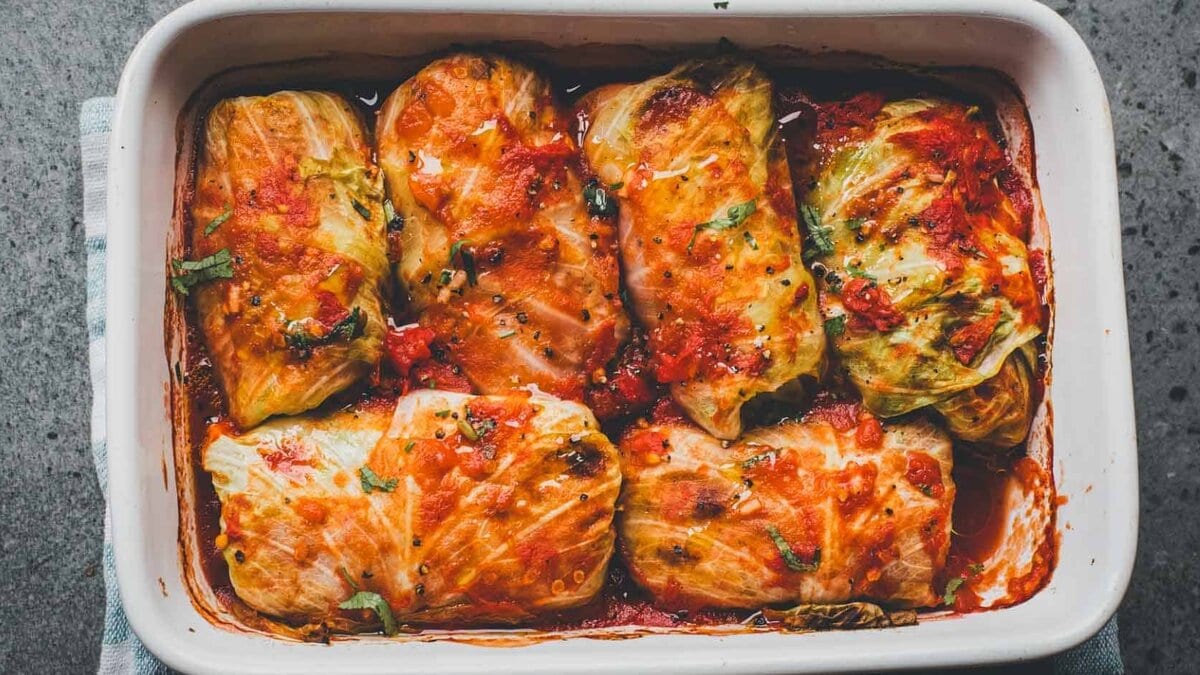 Stuffed cabbage rolls filled with rice and meat in tomato sauce inside a white baking dish.