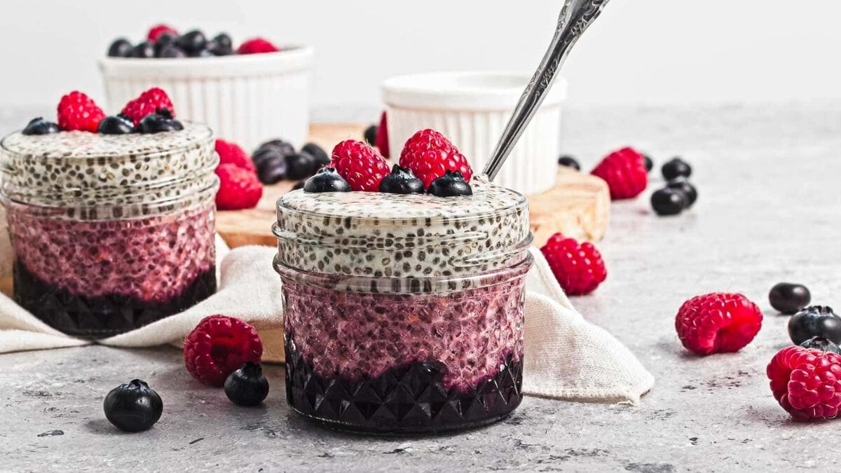 Layered chia pudding in jars topped with raspberries and blueberries, surrounded by scattered berries.
