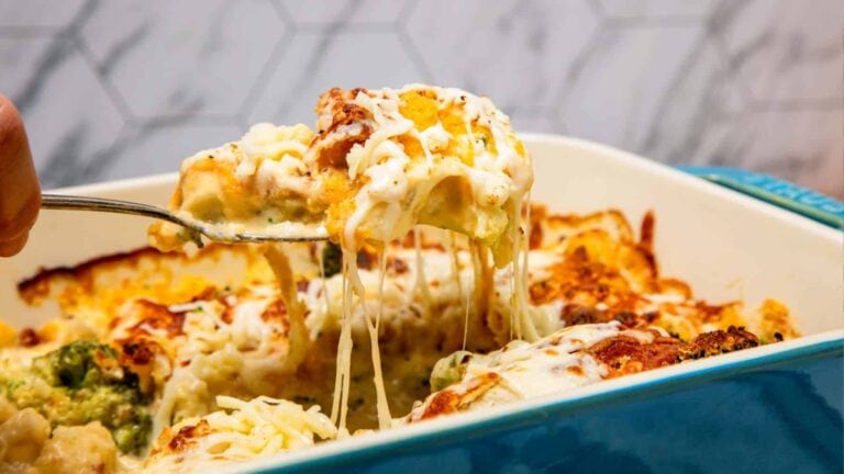 A close-up of a cheesy baked casserole being served from a blue dish, with melted cheese stretching from the portion.