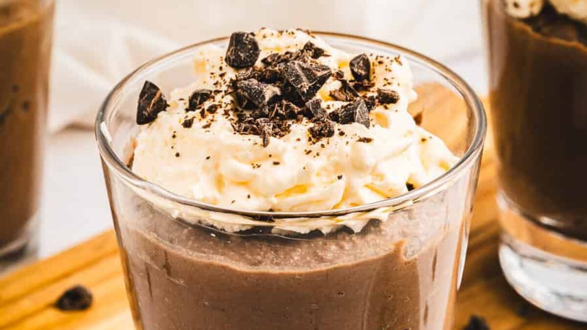 A glass of chocolate mousse topped with whipped cream and chocolate shavings.